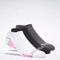 Three pairs of Reebok Women's Zoned Cushion No-Show Socks are shown overlapping on a white background: one white with pink and gray accents, one solid black, and one solid gray.