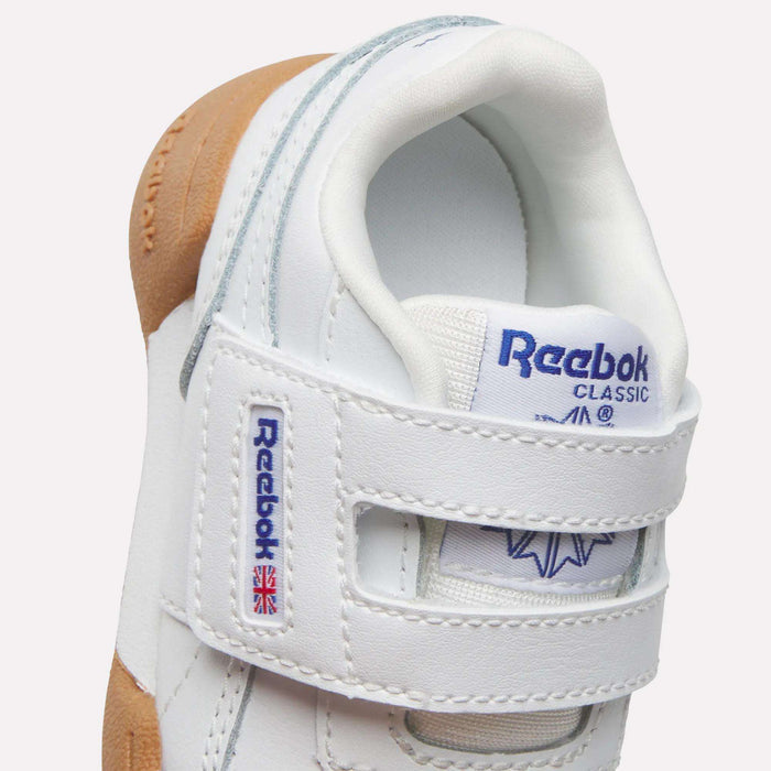 Close-up of Reebok Kids' Workout Plus Shoes for babies and toddlers, featuring white uppers, Velcro straps with brand logo and Union Jack flag, gum-colored sole, and grey accents—ideal for little feet.