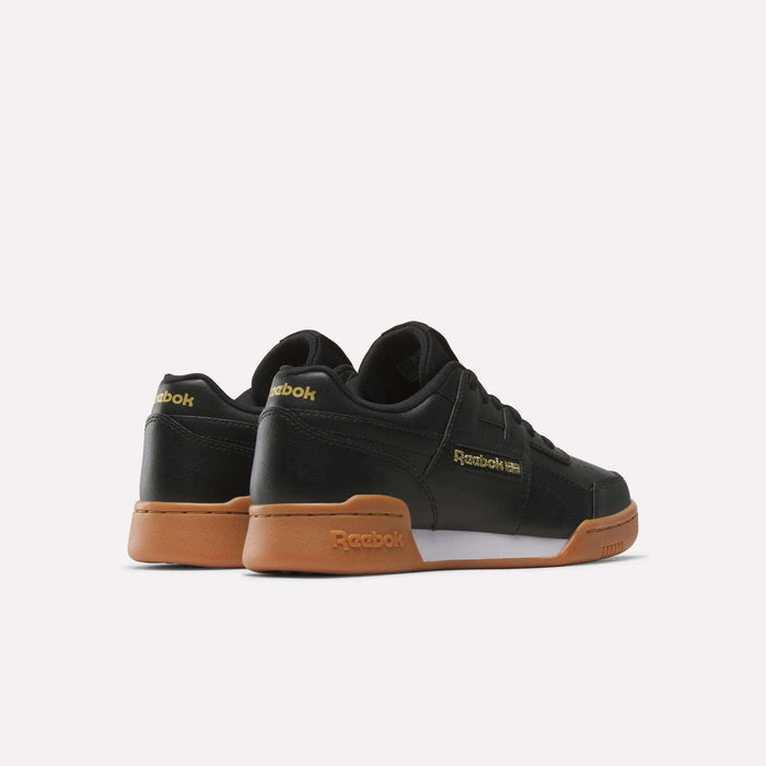 The Reebok Workout Plus Shoes - Big Kids feature a black upper, brown rubber soles, and gold branding. Displayed on a white background, the shoes are angled to reveal both the back and side views.