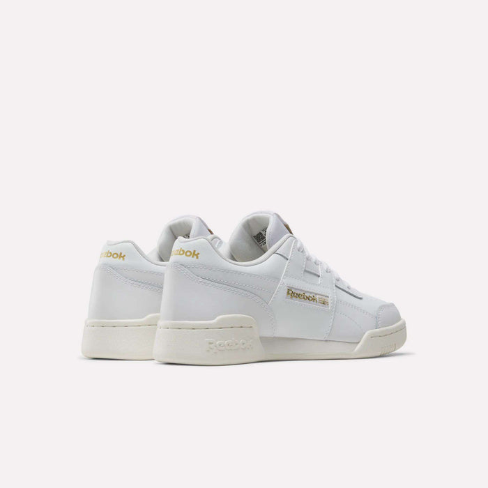 The Reebok Workout Plus Shoes for big kids are shown in white with gold logo accents, viewed from the back and side on a plain white background. These classic, low-top juniors’ sneakers feature off-white soles for timeless style.