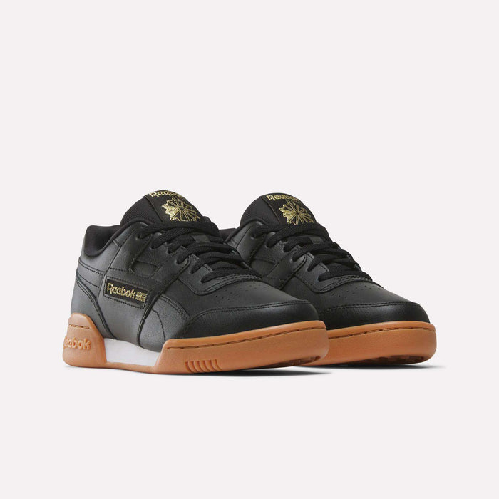 The Reebok Workout Plus Shoes for Big Kids feature gum soles and gold logo details on the sides and tongue. Shown against a white background, these black sneakers add a sleek, sporty touch to any outfit.