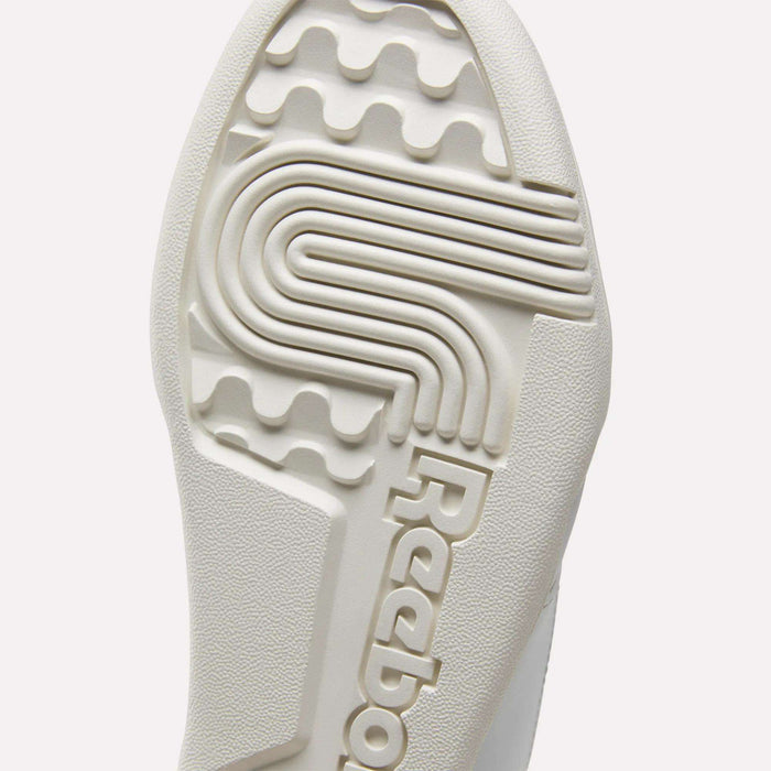 Close-up of the textured sole of white Reebok Workout Plus Shoes for big kids, featuring the brand name and a unique pattern with grooves and ridges for sporty traction.