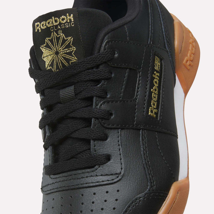 Close-up of black Reebok Workout Plus Shoes for big kids, featuring black laces, gold Reebok branding on the tongue and side, and a brown rubber sole—an eye-catching choice among Reebok footwear.