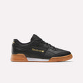 A side-profile of the Reebok Workout Plus Shoes in Black/Gold/Gum is displayed against a plain white background, featuring gold Reebok branding on the side and heel, black laces, and a classic gum sole—showcasing timeless ’80s fitness style.