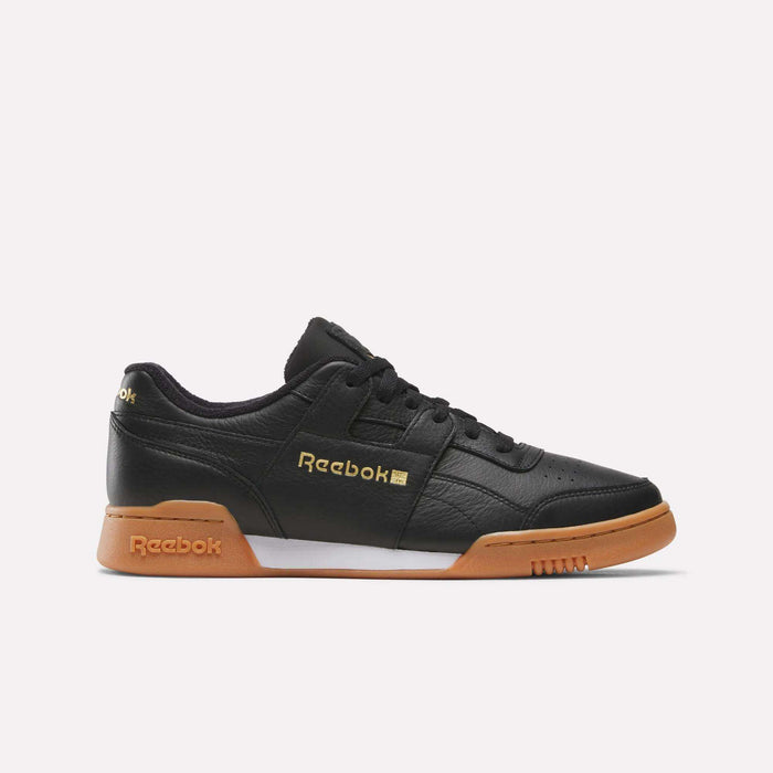 A side-profile of the Reebok Workout Plus Shoes in Black/Gold/Gum is displayed against a plain white background, featuring gold Reebok branding on the side and heel, black laces, and a classic gum sole—showcasing timeless ’80s fitness style.