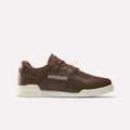 A Formal Brown/Ftwr White/Chalk Reebok Workout Plus Shoe featuring a white sole, iconic side logo patch, brown laces, and a low-top silhouette is presented in profile against a plain white background—these classic sneakers embody the timeless style of the Workout Plus line.