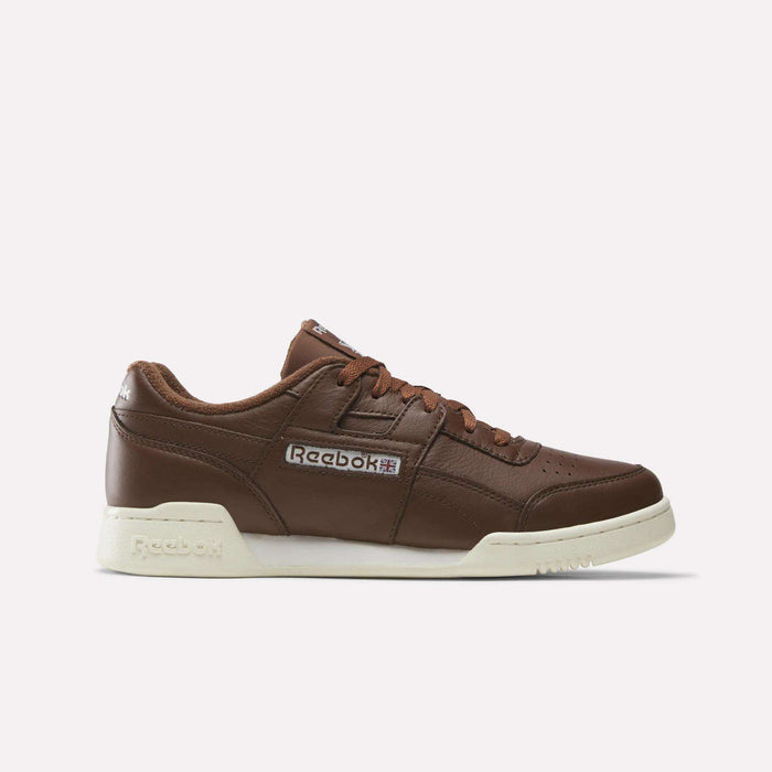 A Formal Brown/Ftwr White/Chalk Reebok Workout Plus Shoe featuring a white sole, iconic side logo patch, brown laces, and a low-top silhouette is presented in profile against a plain white background—these classic sneakers embody the timeless style of the Workout Plus line.