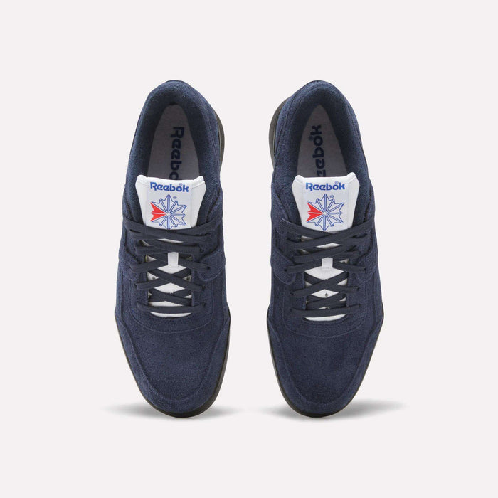 A pair of Reebok Workout Plus Shoes in navy blue with white laces and soles, featuring the Reebok logo and a red-blue star on the white tongue, capture classic '80s style against a light background.