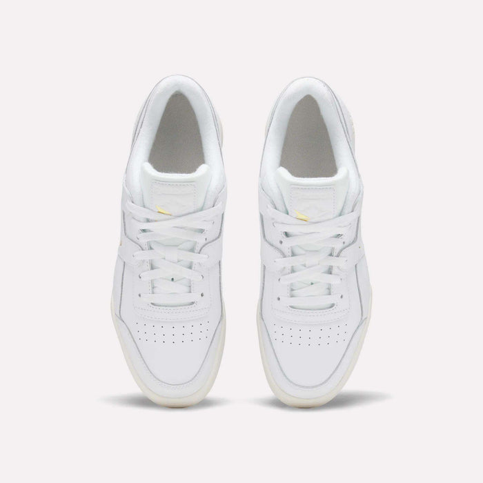 A pair of Reebok Workout Plus Shoes in white, featuring white laces, light yellow accents, perforated toe boxes, and cream outsoles, are seen from above on a plain background for an '80s-inspired look.
