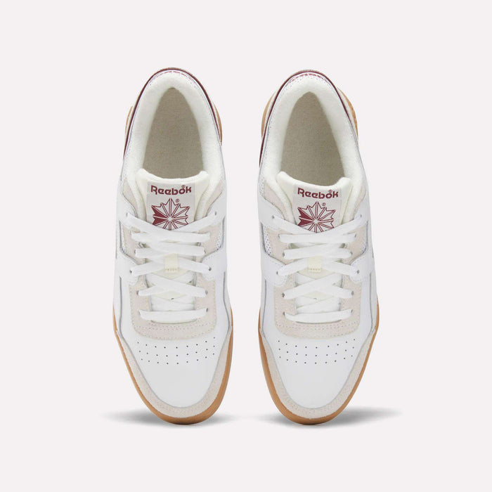 Top view of Reebok Workout Plus Shoes in white with gum soles, maroon Reebok logos on the tongues, and perforated toe boxes, evoking classic '80s fitness style against a light background.