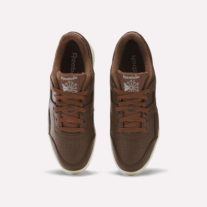 Top view of a pair of brown Reebok Workout Plus Shoes with matching brown laces, cream-colored soles, and the Reebok logo visible on each tongue against a plain white background—timeless sneakers perfect for any wardrobe.