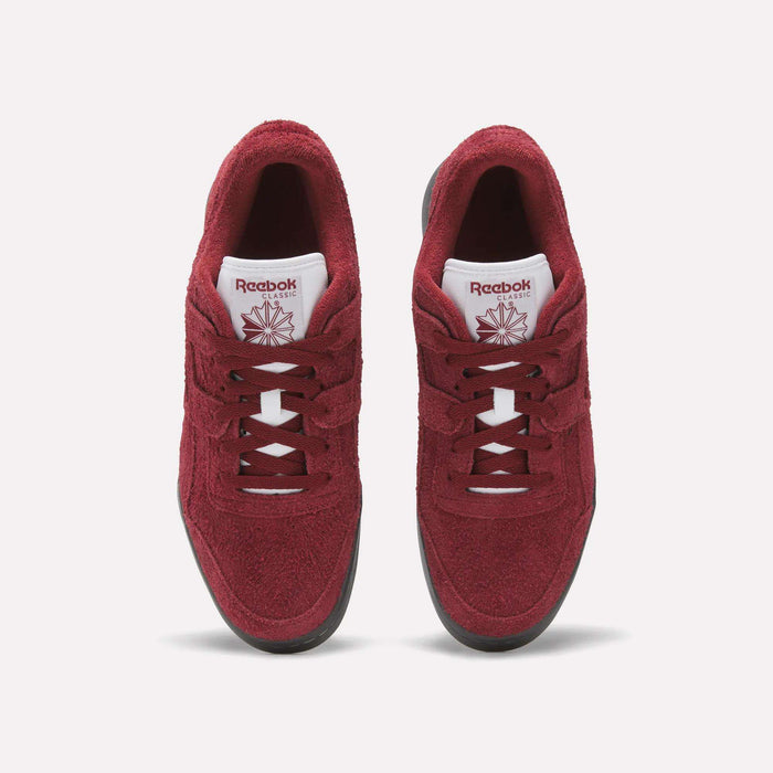 A pair of red Reebok Workout Plus Shoes with white tongues, black soles, and matching red laces and logos is shown from above on a plain white background, highlighting the classic fitness style.