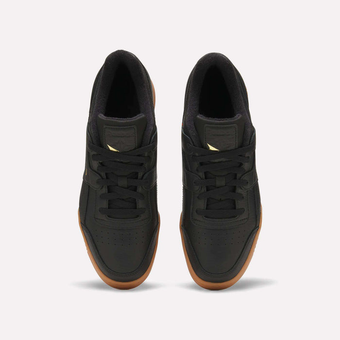 A pair of Reebok Workout Plus Shoes in black with gum soles, seen from above on a white background. Featuring black laces and a small gold Reebok logo on the tongue, these shoes evoke subtle ’80s fitness style reminiscent of the classic era.