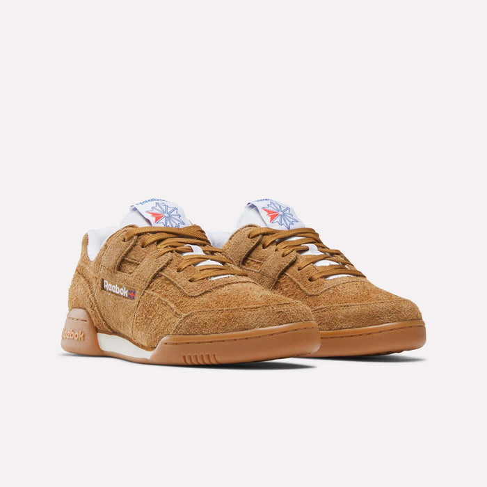A pair of tan suede Reebok Workout Plus Shoes with gum soles, white midsoles, and side Reebok logos. The tongue displays a white patch with a blue and red star, channeling '80s style. Shown on a plain white background.
