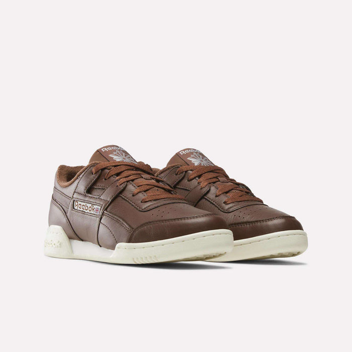 A pair of brown Reebok Workout Plus Shoes with white soles and brown laces, displayed on a plain white background—timeless footwear from Reebok, perfect for any occasion.