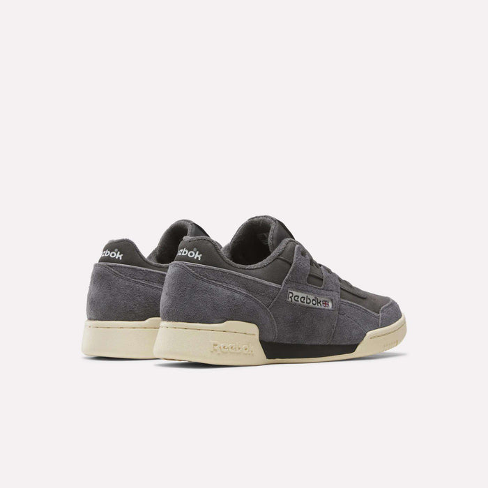 A pair of Reebok Workout Plus Shoes in dark gray suede with off-white soles, shown from the back and side on a plain light background. Archive-inspired, these shoes combine classic style with modern comfort.