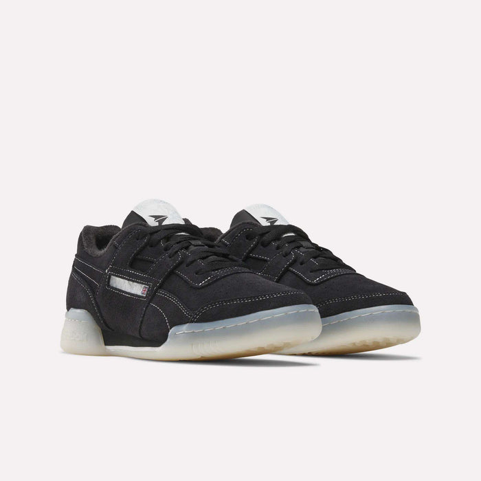The Reebok Workout Plus Shoes are black low-tops with white stitching, translucent rubber soles, and black laces, capturing classic '80s fitness style against a simple light background.