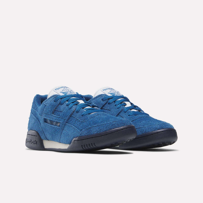 The Reebok Workout Plus Shoes feature textured blue fabric, black soles, white midsoles, and tongue labels with the Reebok logo, capturing ‘80s fitness style against a plain white background.