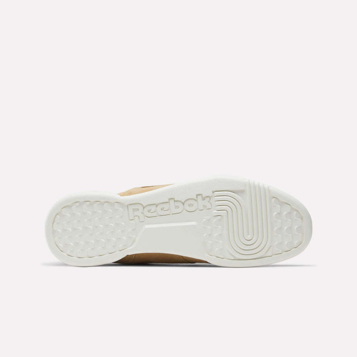 The image shows the white rubber sole of Reebok Workout Plus Shoes from the bottom, featuring textured patterns and an embossed Reebok logo at the center. The plain light pink background evokes classic '80s fitness style.