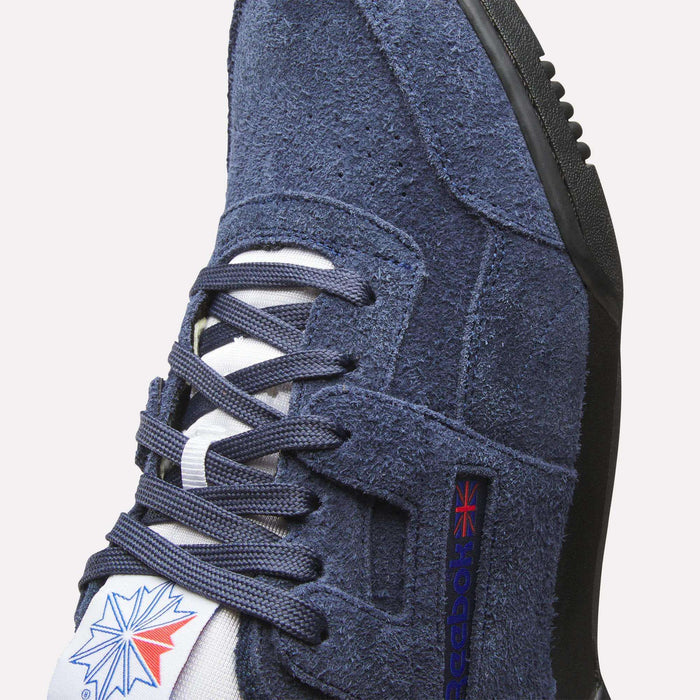 Close-up of Reebok Workout Plus Shoes in navy suede, featuring blue laces, a white tongue with the Reebok logo and Union Jack flag—classic 80s fitness style.