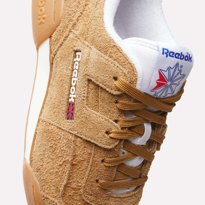 A close-up of tan suede Reebok Workout Plus Shoes with brown laces, a white tongue showing the Reebok logo and Union Jack, and a white and gum sole. Classic '80s fitness style is highlighted with visible stitching and textured suede.