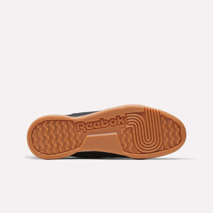 The image displays the sole of the Reebok Workout Plus Shoes, showcasing a gum-colored base with both wavy and linear tread patterns, as well as the Reebok logo embossed at the center—highlighting the iconic ’80s fitness-inspired style characteristic of these classic workout shoes.