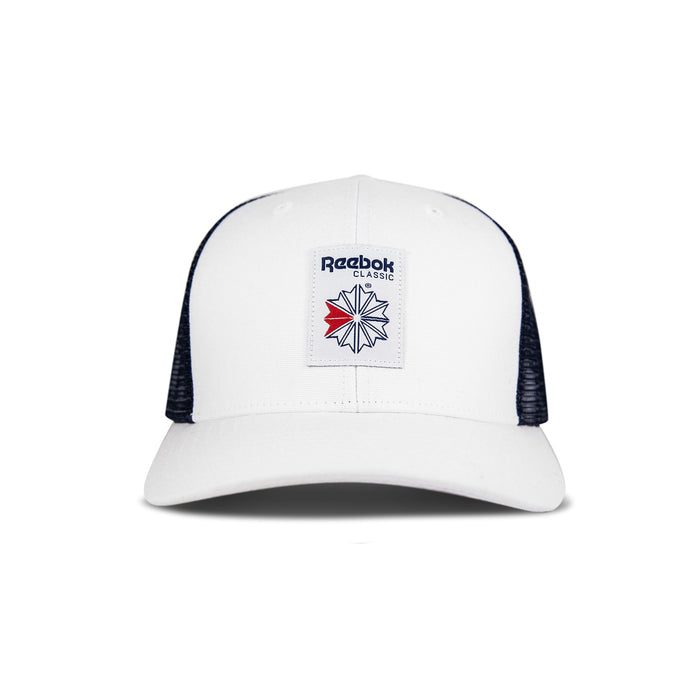 The Reebok Woven Patch Vector Trucker Cap is white with black mesh sides, a curved brim, and a navy/red logo patch. This adjustable snapback is shown on a plain white background.