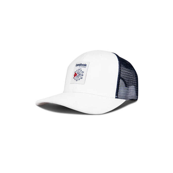 The Reebok Woven Patch Vector Trucker Cap features a white front, navy mesh back, adjustable snapback, and a rectangular patch with the red and blue star logo on the front.