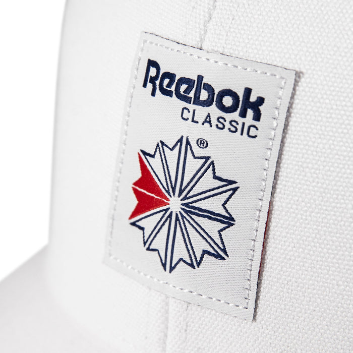 Close-up of the Woven Patch Vector Trucker Cap by Reebok, showcasing a bold woven patch with the classic blue and red geometric star logo and navy text.