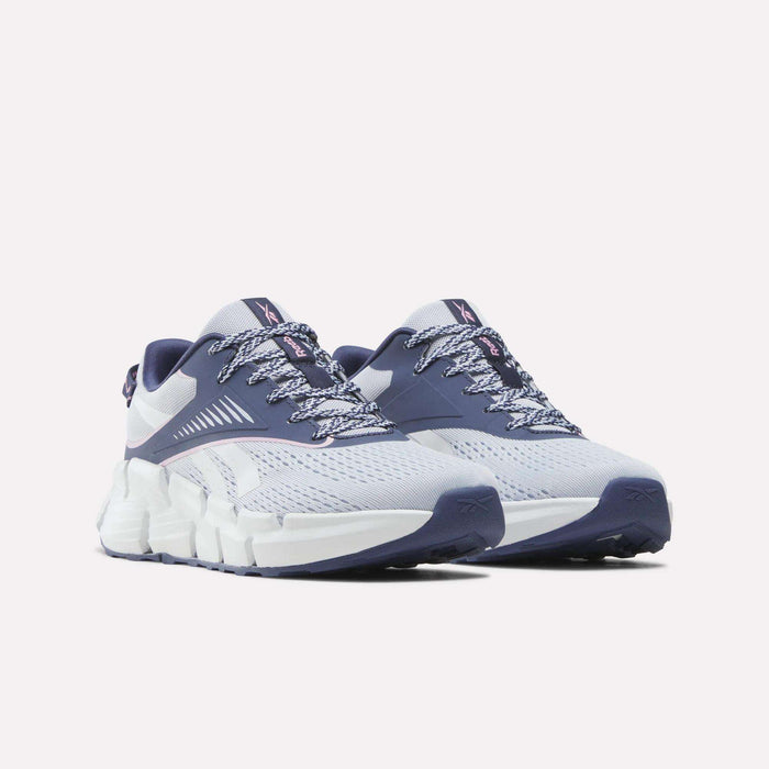 A pair of Reebok Zig Dynamica 6 Running Shoes for Big Kids in white and purple, featuring patterned laces, breathable mesh uppers, and chunky white soles with innovative Zig technology, displayed against a plain white background.
