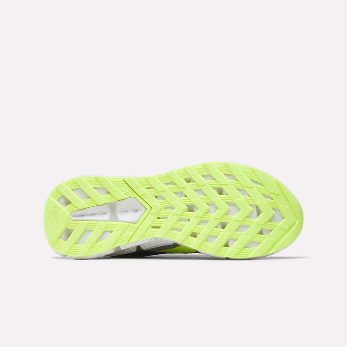 The image shows the bottom view of Reebok Zig Dynamica 6 Running Shoes for big kids, featuring a bright yellow-green patterned rubber sole with a geometric tread, lying flat on a white background.